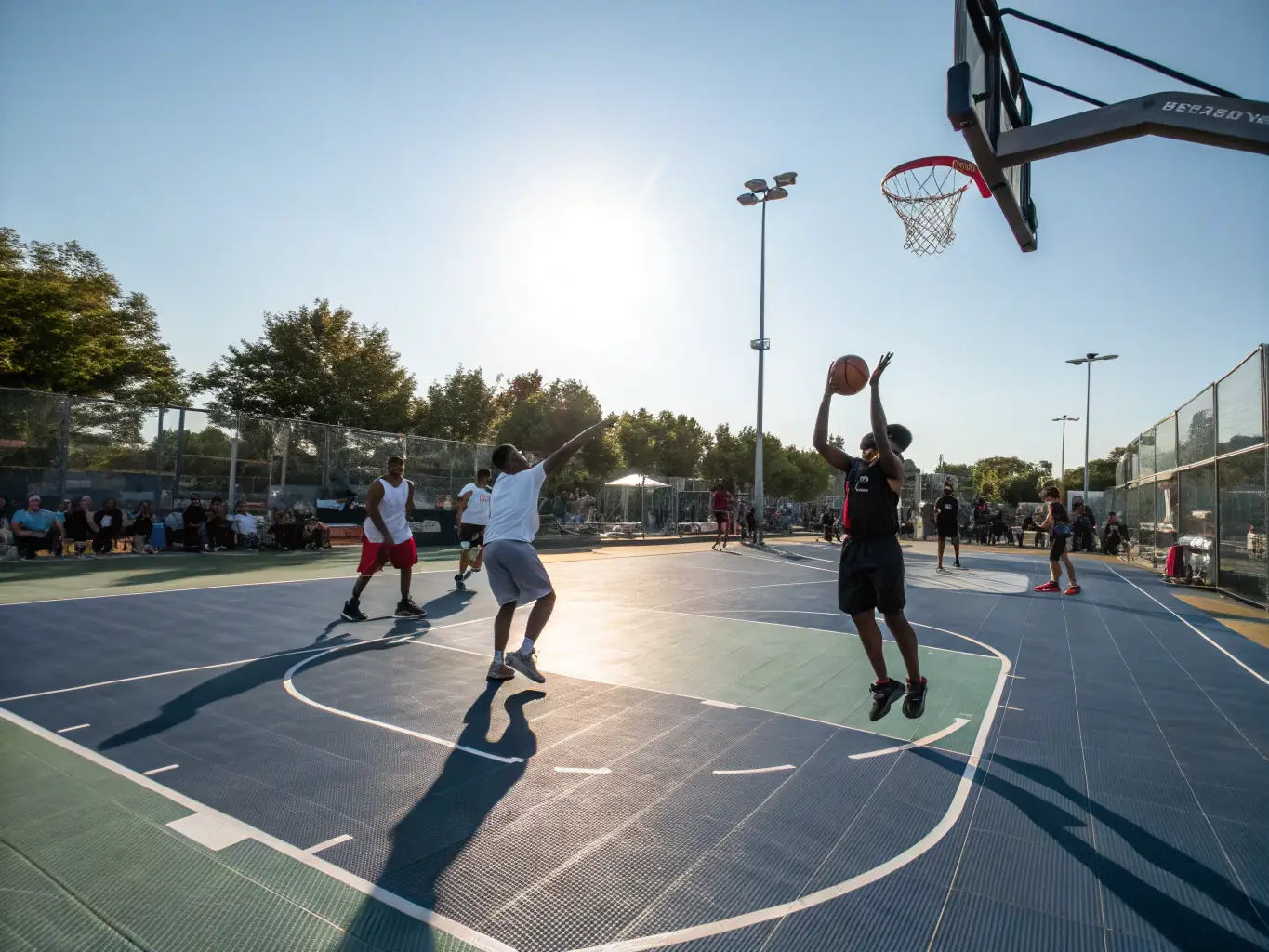 A group of adult basketball players engaged in a friendly scrimmage on an outdoor court during a sunny day. The image conveys a sense of community and active lifestyle.